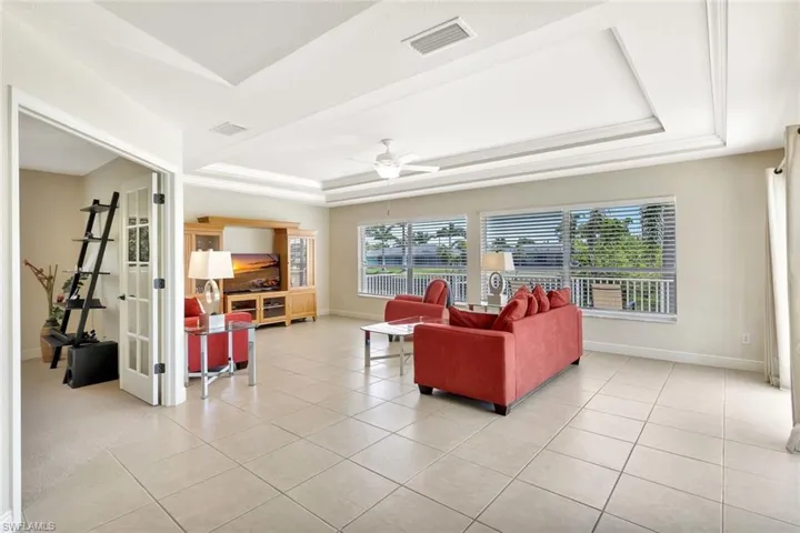 Living room featuring a raised ceiling, baseboards, a ceiling fan, and light tile patterned floors
