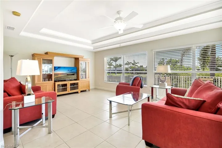 Living room with a raised ceiling, ceiling fan, light tile patterned flooring, and baseboards