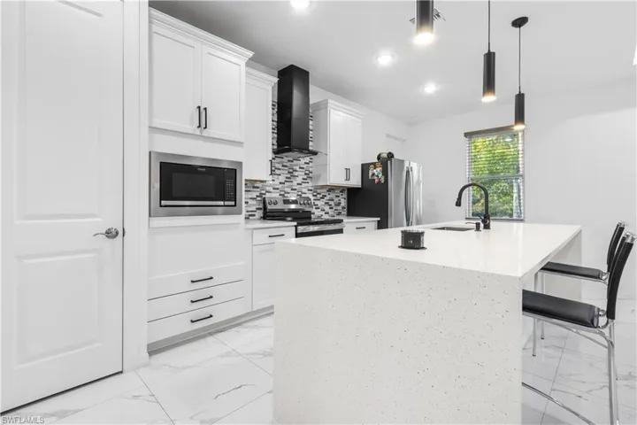Kitchen featuring a center island with sink, decorative light fixtures, stainless steel appliances, light stone counters, and a breakfast bar area