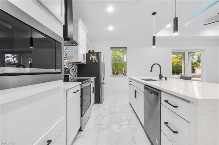 Kitchen with white cabinets, stainless steel appliances, decorative light fixtures, light stone counters, and light marble finish floors