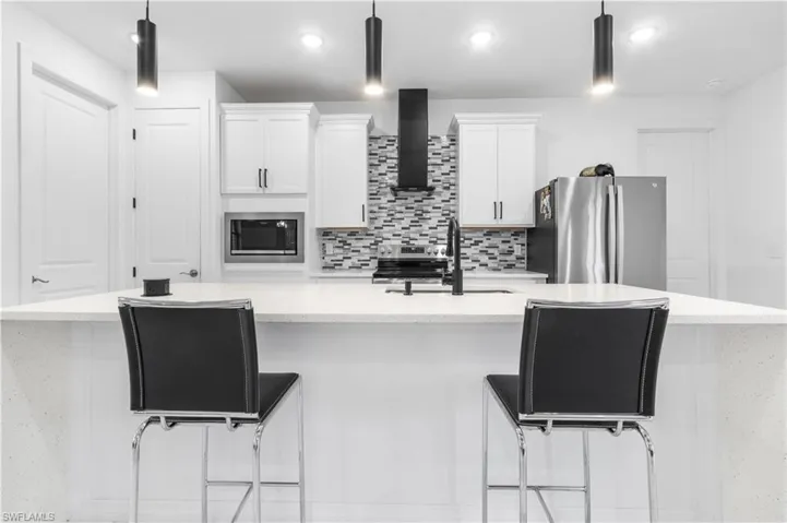 Kitchen featuring a kitchen breakfast bar, a spacious island, white cabinets, light stone counters, and stainless steel appliances