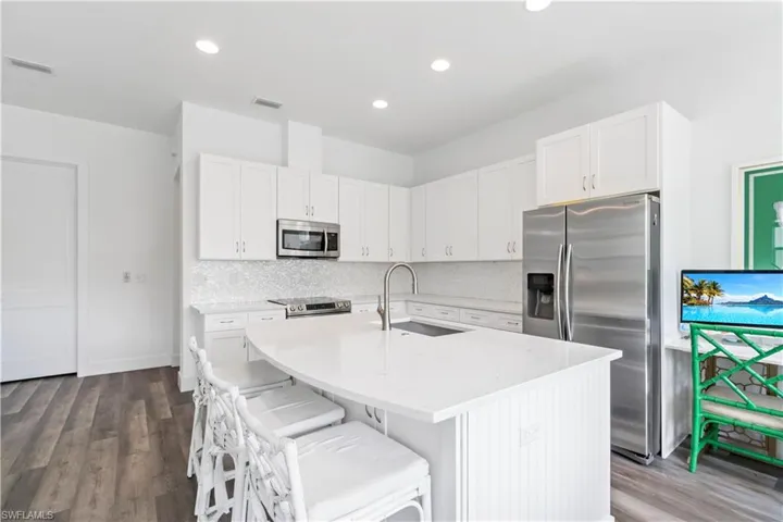 Kitchen featuring stainless steel appliances, an island with sink, a kitchen bar, white cabinetry, and sink