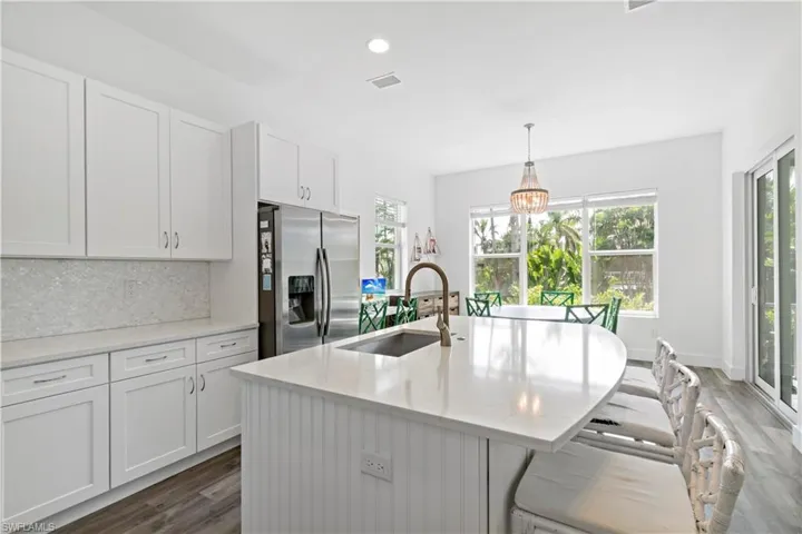 Kitchen with a center island with sink, stainless steel fridge with ice dispenser, pendant lighting, sink, and white cabinetry