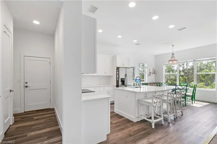 Kitchen with a center island with sink, stainless steel fridge, tasteful backsplash, a kitchen bar, and white cabinetry