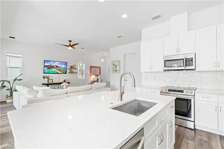 Kitchen featuring stainless steel appliances, sink, ceiling fan, light stone countertops, and a kitchen island with sink