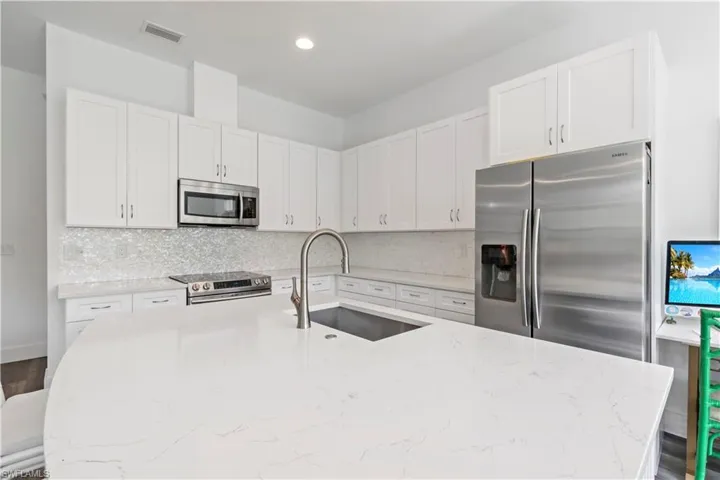 Kitchen featuring light stone counters, a kitchen bar, white cabinetry, appliances with stainless steel finishes, and sink