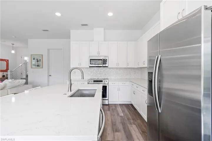 Kitchen featuring light stone countertops, decorative backsplash, white cabinetry, appliances with stainless steel finishes, and sink
