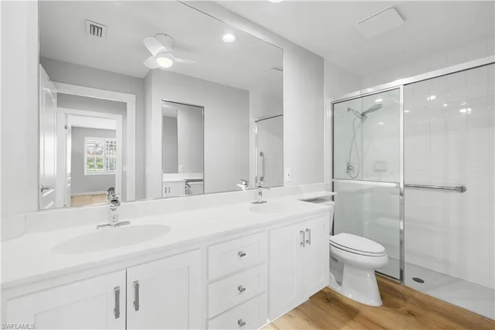 Full bath featuring a shower stall, toilet, double vanity, wood finished floors, and recessed lighting