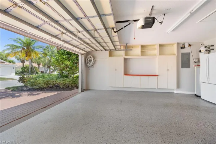 Garage featuring electric panel, freestanding refrigerator, a garage door opener, and epoxy floor