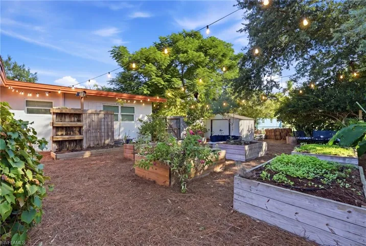 Backyard featuring raised wooden garden beds, overhead string lighting, a detached storage shed, and mature perimeter trees