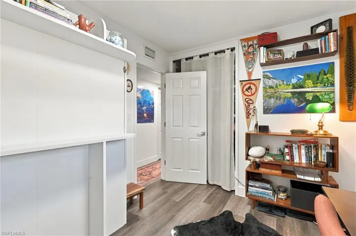 Wood-finish flooring throughout, white built-in wall cabinetry with overhead shelving, and a classic six-panel interior door