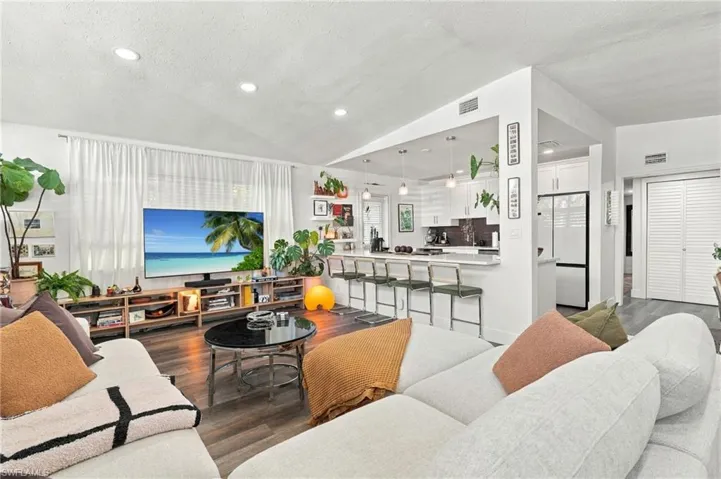 Open-concept interior featuring vaulted ceilings, recessed lighting, wood-finish flooring, and a kitchen breakfast bar with pendant lighting