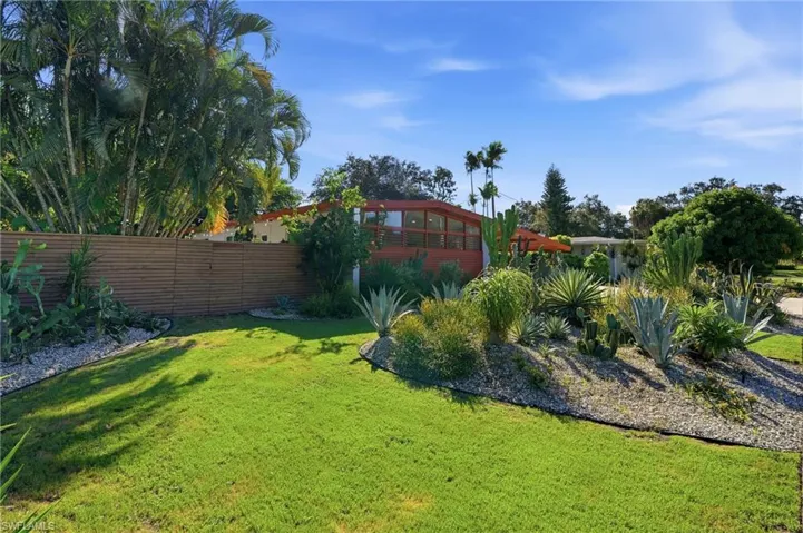 Mid-century modern exterior featuring clerestory windows, horizontal wood-slat privacy fencing, xeriscaped landscape design, and mature palm trees