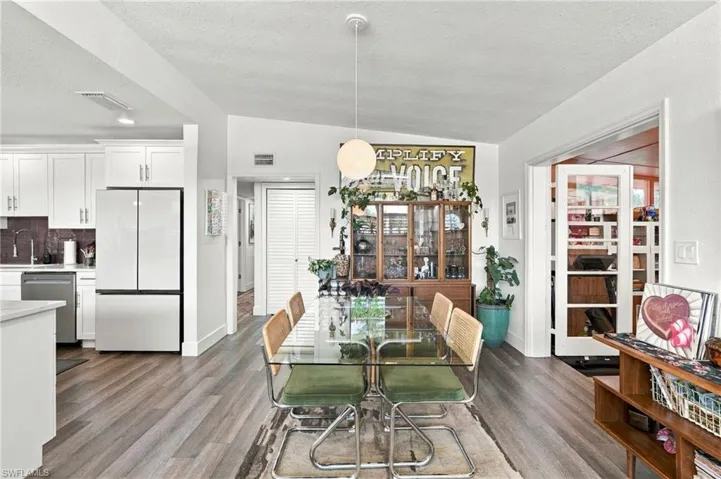 Open-concept kitchen and dining area featuring wood-finish flooring, white shaker-style cabinetry, stainless steel appliances, and a glass-paneled door