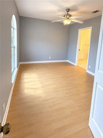 Arched window providing natural light, wood-finish flooring, ceiling fan with integrated lighting, and a white paneled door