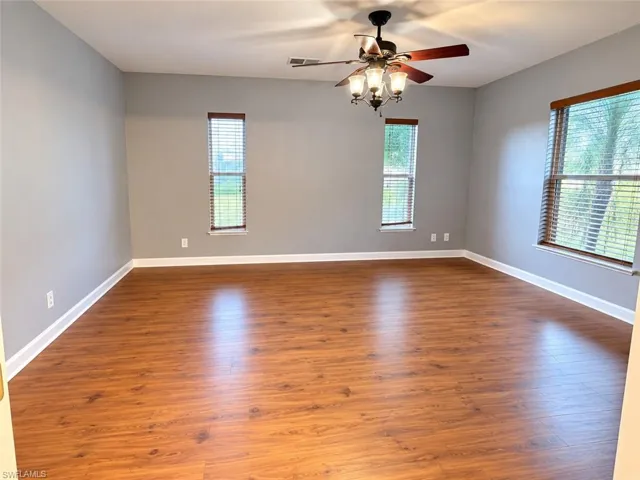 Spacious room featuring wood-finish flooring, light gray walls, multiple windows with blinds, and a ceiling fan with integrated lighting