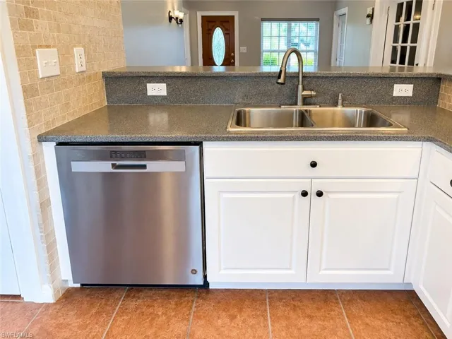 Stainless steel dishwasher, dual basin sink with gooseneck faucet, white cabinetry with dark hardware, stone-finish countertops, and subway tile backsplash
