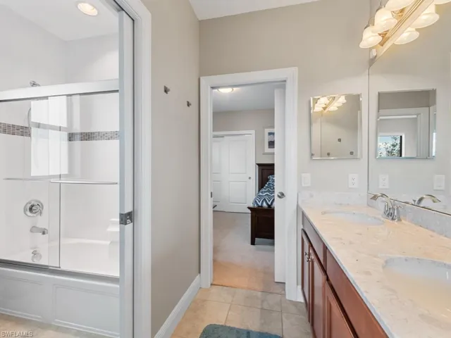 Full bath featuring tile patterned flooring, connected bathroom, bath / shower combo with glass door, a sink, and double vanity