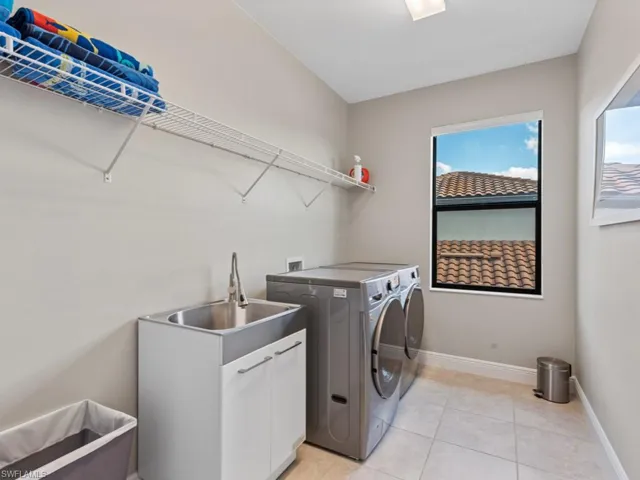 Laundry room featuring light tile patterned flooring, a sink, baseboards, washer and dryer, and cabinet space