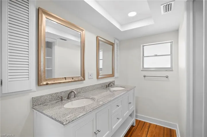 Bathroom with double vanity, dark wood-type flooring, a tray ceiling, and recessed lighting