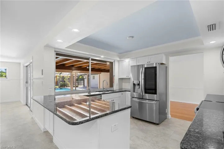 Kitchen featuring dark stone counters, stainless steel fridge with ice dispenser, a peninsula, recessed lighting, and white cabinets