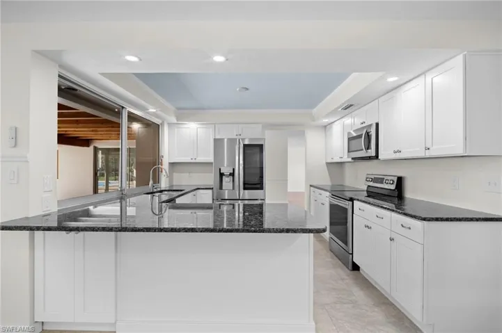 Kitchen featuring a raised ceiling, stainless steel appliances, dark stone counters, a peninsula, and recessed lighting