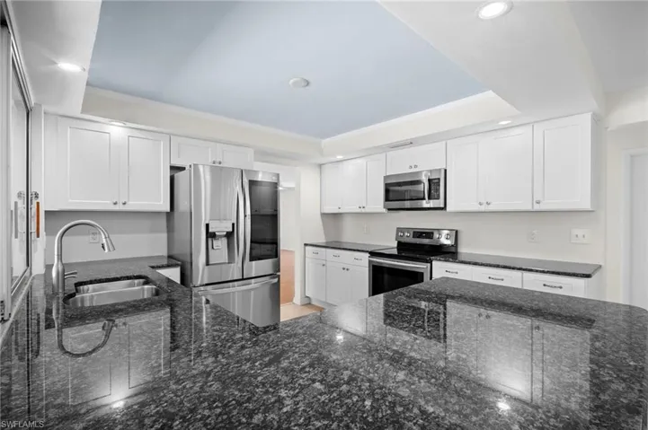 Kitchen with dark stone counters, stainless steel appliances, white cabinets, crown molding, and recessed lighting