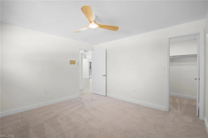 Unfurnished bedroom featuring a spacious closet, light colored carpet, and ceiling fan
