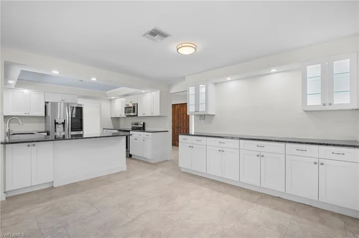 Kitchen with stainless steel appliances, white cabinetry, dark stone counters, recessed lighting, and glass insert cabinets