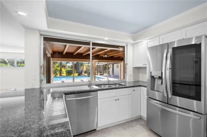 Kitchen with stainless steel appliances, dark stone countertops, white cabinets, ornamental molding, and recessed lighting