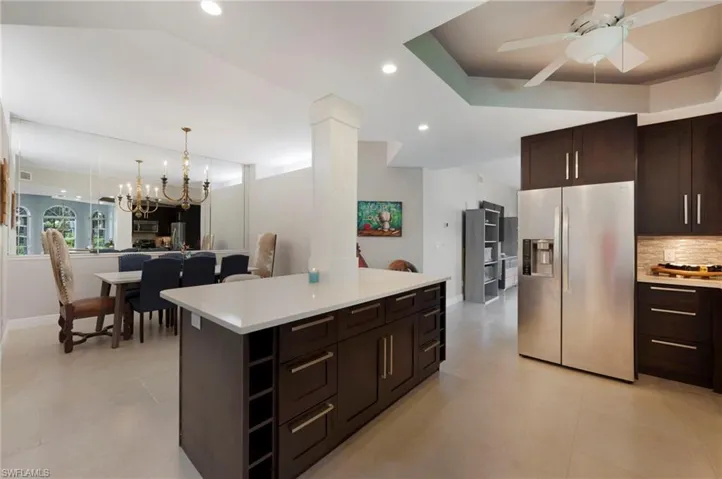 Kitchen with ceiling fan with notable chandelier, a kitchen island, appliances with stainless steel finishes, light tile floors, and pendant lighting