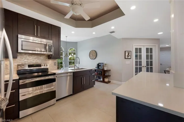 Kitchen with a tray ceiling, tasteful backsplash, stainless steel appliances, light tile floors, and sink