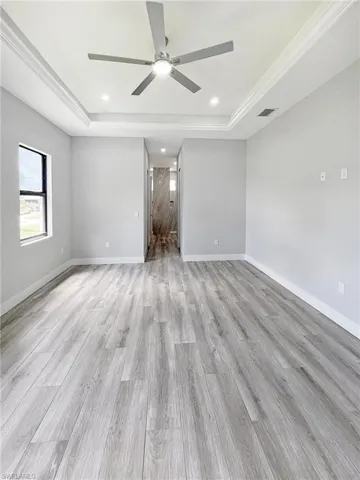 Empty room with a raised ceiling, ceiling fan, light wood-style floors, recessed lighting, and ornamental molding