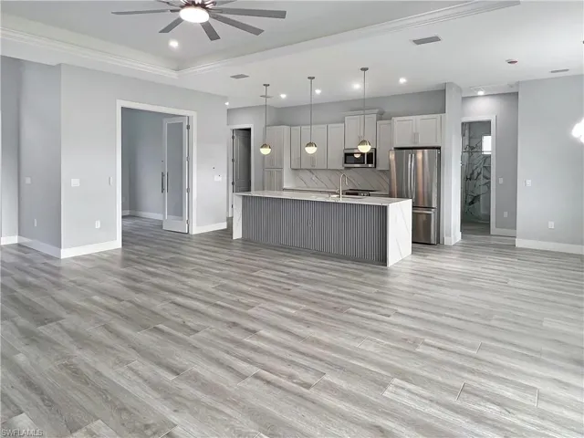 Kitchen featuring open floor plan, hanging light fixtures, stainless steel appliances, white cabinets, and a kitchen island with sink