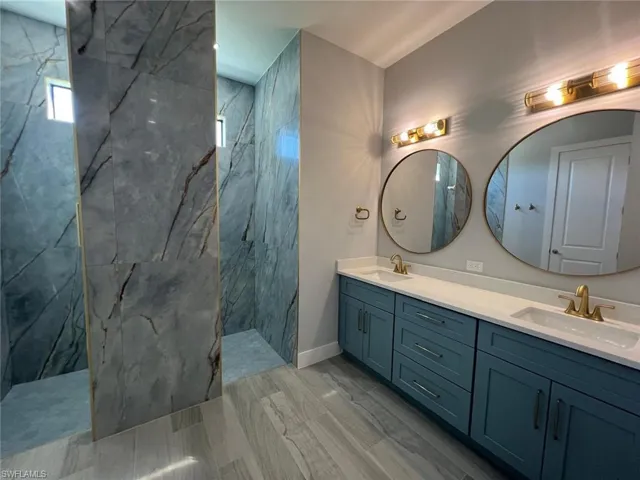 Bathroom with double vanity, a marble finish shower, and wood finish floors