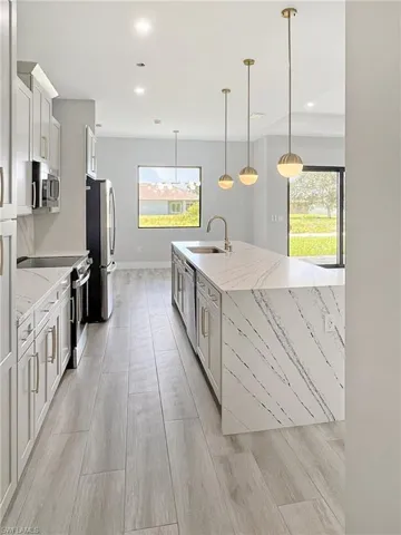 Kitchen featuring stainless steel appliances, light stone counters, light wood-type flooring, pendant lighting, and white cabinets