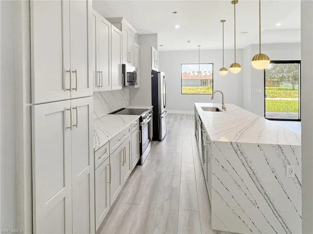 Kitchen featuring open floor plan, stainless steel appliances, a kitchen island with sink, hanging light fixtures, and a ceiling fan