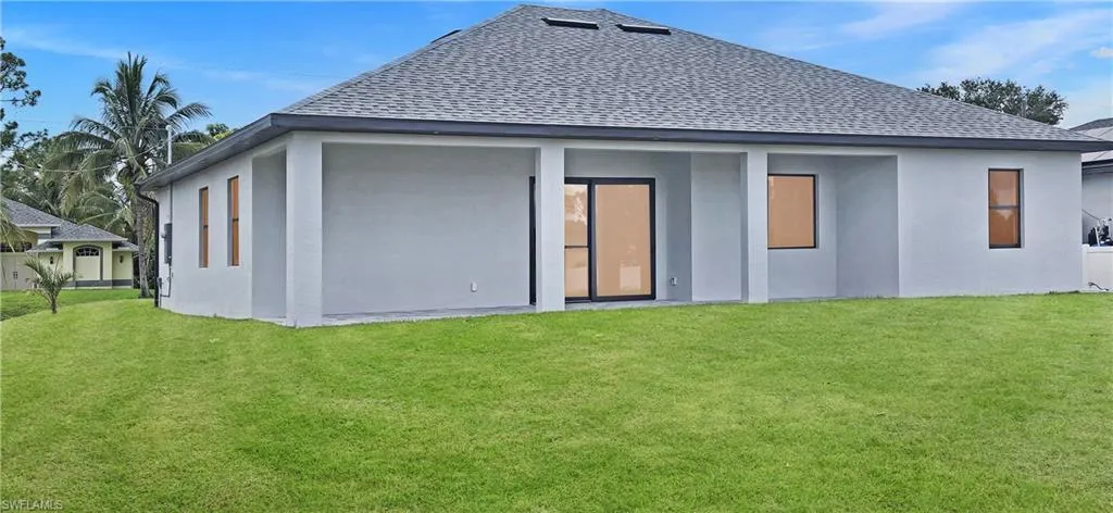 Rear view of house featuring roof with shingles, a yard, and stucco siding