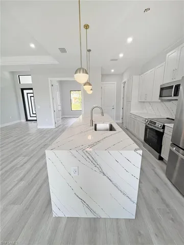 Kitchen featuring pendant lighting, an island with sink, stainless steel appliances, light wood-style flooring, and light stone countertops