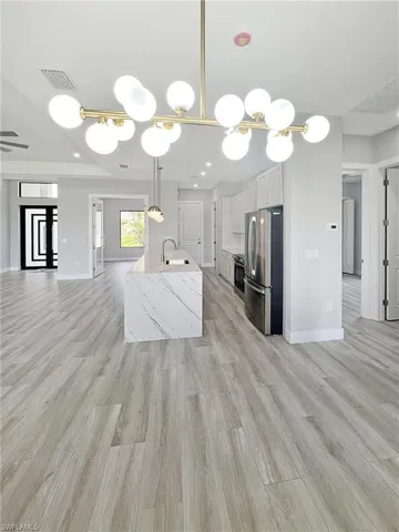 Kitchen with an island with sink, stainless steel appliances, light wood-style flooring, suspended lighting, and light stone countertops