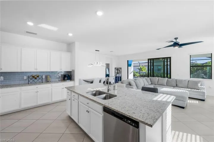 Kitchen with white cabinetry, light stone countertops, dishwasher, and hanging light fixtures
