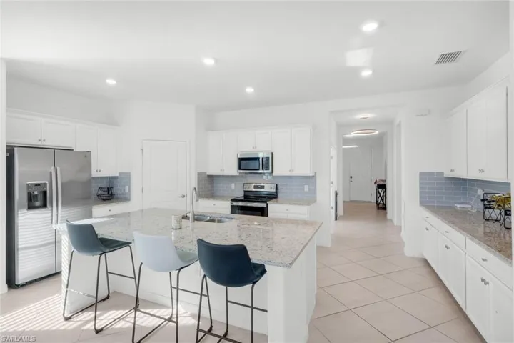 Kitchen with white cabinetry, stainless steel appliances, light stone countertops, a kitchen bar, and recessed lighting