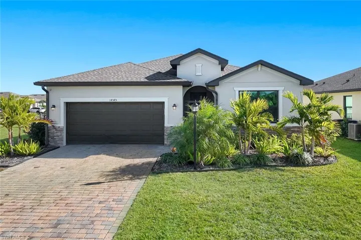 View of front facade with stucco siding, a front yard, decorative driveway, and stone siding