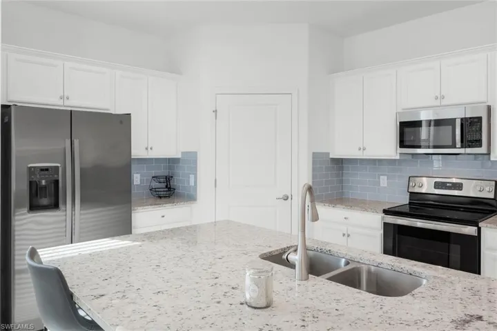 Kitchen with stainless steel appliances, white cabinets, light stone counters, and backsplash