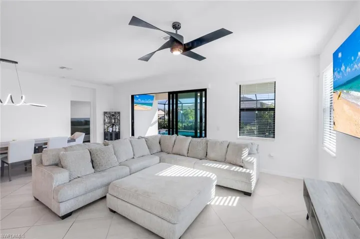 Living room with healthy amount of natural light, light tile patterned floors, suspended lighting, and a ceiling fan