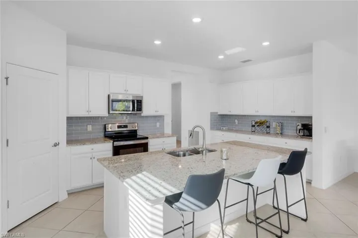 Kitchen with white cabinetry, stainless steel appliances, a breakfast bar area, light stone counters, and light tile patterned flooring