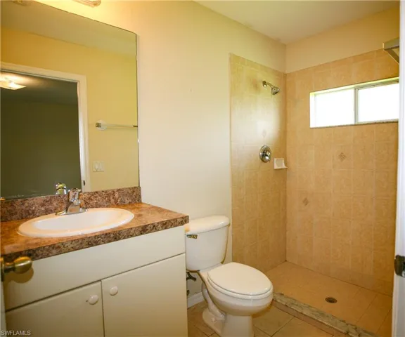 Bathroom featuring a single vanity with a laminate countertop and an integrated sink, a toilet, and a tiled shower stall with a small window
