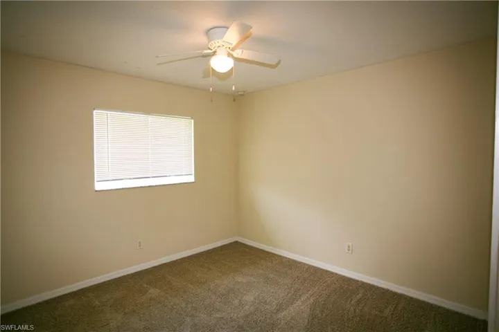 The room features plush carpeted flooring, a window with horizontal blinds, and a ceiling fan with an integrated light fixture