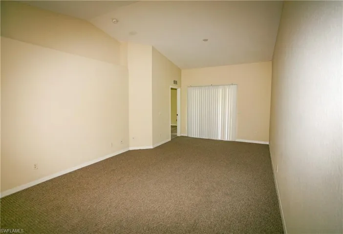 Spacious room featuring carpeting, neutral-toned walls, and a sliding glass door with vertical blinds