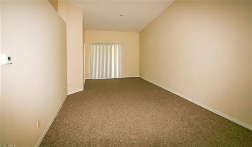 Expansive living area featuring neutral-toned carpet, light-colored walls, and a sliding glass door with vertical blinds